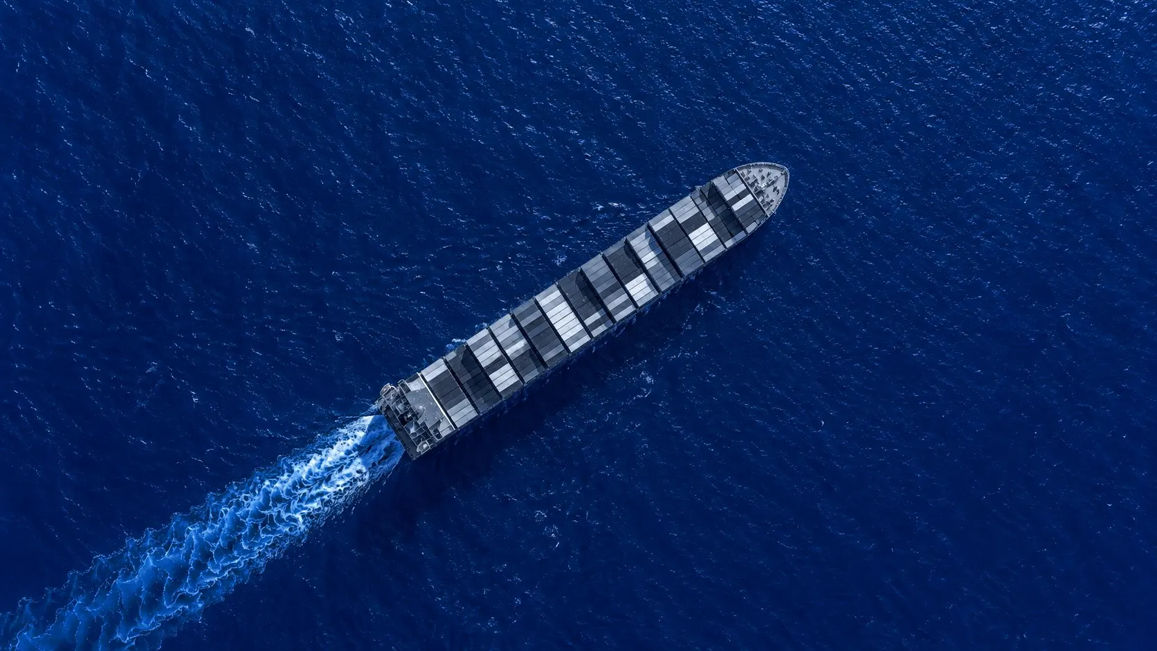 Container ship seen from directly above, with its white wake on dark blue sea