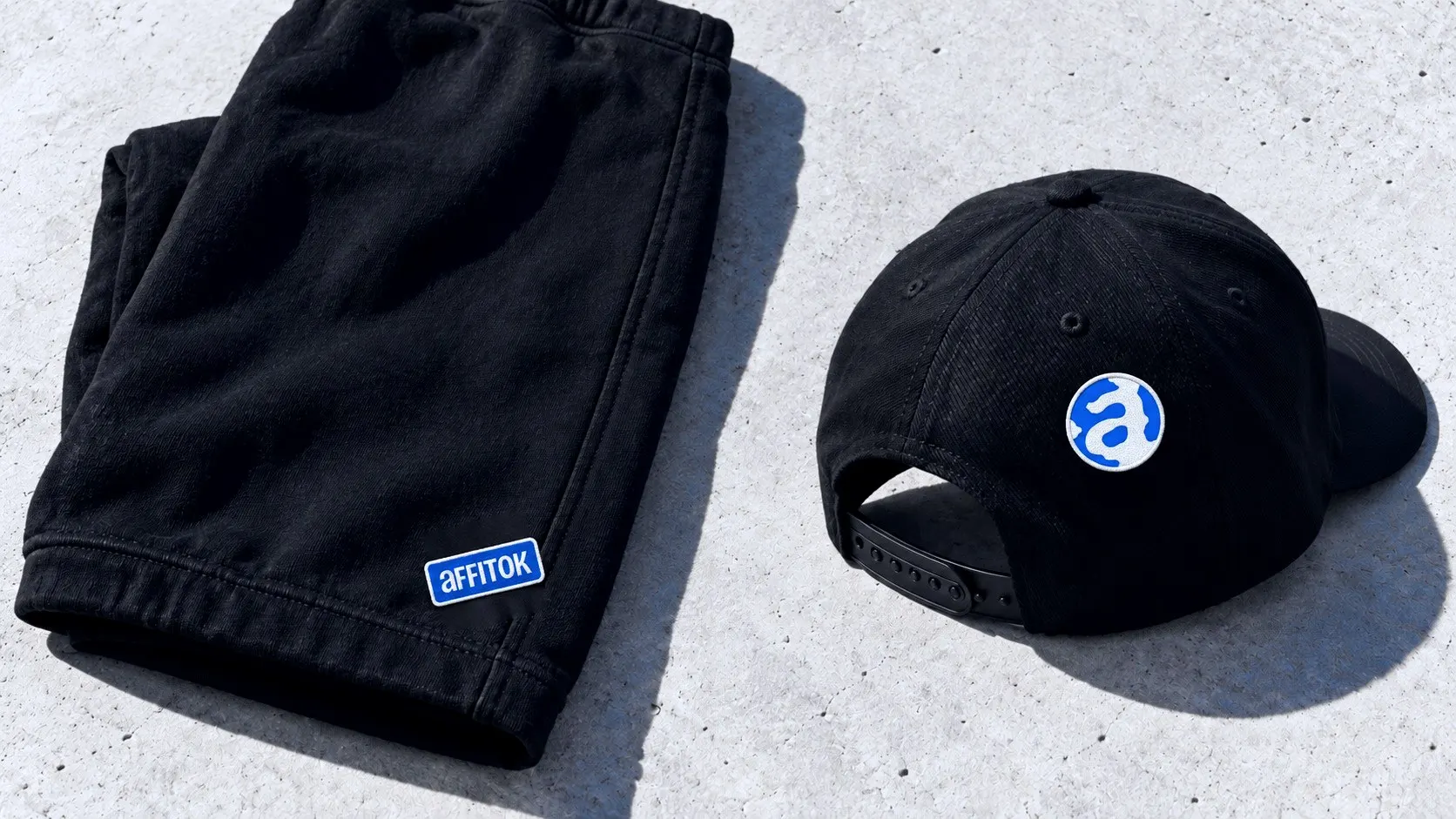 Black sweatpants with an embroidered affitok patch on the hem and a cap with a round embroidered globe patch on the back panel