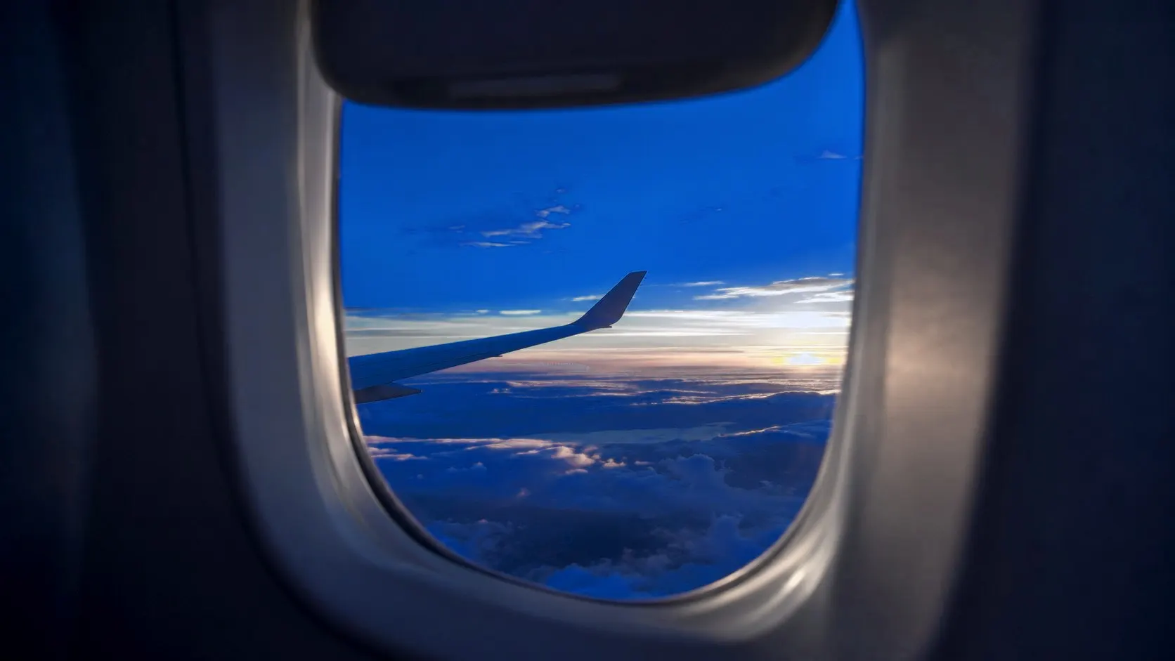 View from an airplane window seat at sunset, the wing tip over the clouds